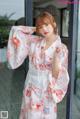 A woman wearing a white kimono standing in front of a window.