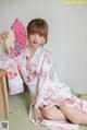 A woman in a kimono sitting on the floor holding a fan.