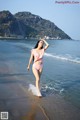 A woman in a pink bikini walking on the beach.