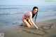 A woman in a pink bikini writing in the sand on the beach.