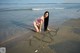 A woman in a pink bikini writing in the sand on the beach.