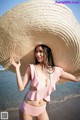 A woman in a pink bikini and a straw hat on the beach.