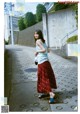 A woman walking down a sidewalk wearing a skirt and sandals.