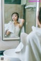 A woman standing in front of a mirror holding a towel over her head.