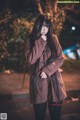 A woman with long black hair standing in the street at night.