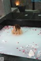 A woman sitting in a bathtub filled with rose petals.