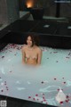 A naked woman sitting in a bathtub filled with rose petals.