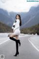 A woman in a white dress and black boots standing on a road.