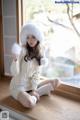 A woman in a white sweater and hat sitting on a window sill.