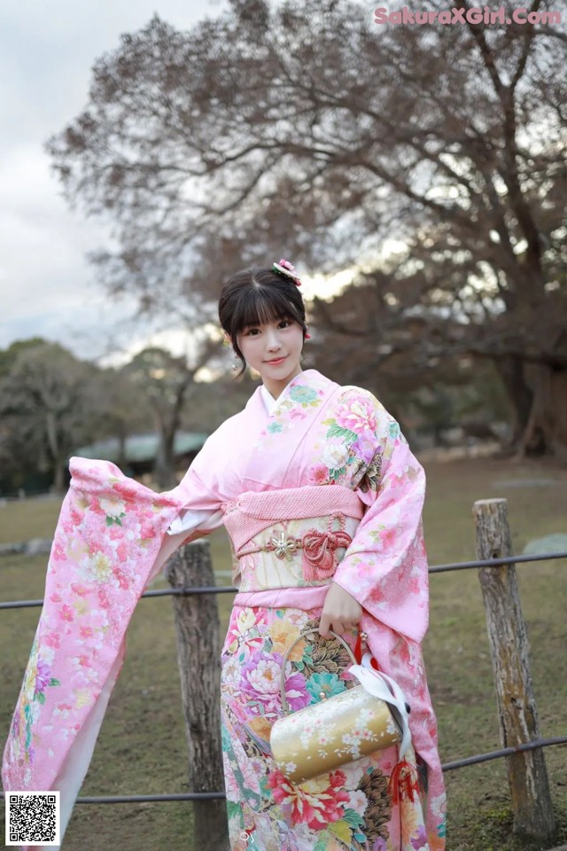 A woman in a pink kimono standing next to a fence.