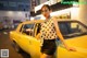 A woman leaning on the hood of a yellow taxi.