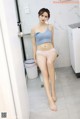 A woman in a blue top and pink panties sitting on a toilet.