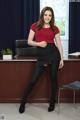 A woman in a red shirt and black skirt posing in front of a desk.