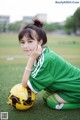 A young woman sitting on the ground with a soccer ball.