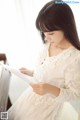 A woman in a white dress reading a piece of paper.