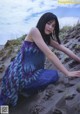 A woman in a blue and purple dress sitting on a sandy beach.