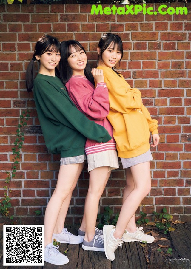 A group of three young women standing next to a brick wall.