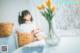 A woman sitting on a bed next to a vase of flowers.