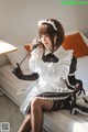 A woman in a maid outfit sitting on a bed holding a broom.