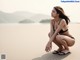 A woman in a black bikini sitting on a beach.