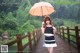 A woman standing on a wooden bridge holding an umbrella.