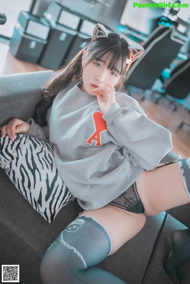 A woman sitting on a couch wearing a gray sweatshirt and black stockings.
