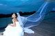 A woman in a wedding dress sitting on a dock.