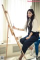 A woman sitting on a stool painting on a easel.